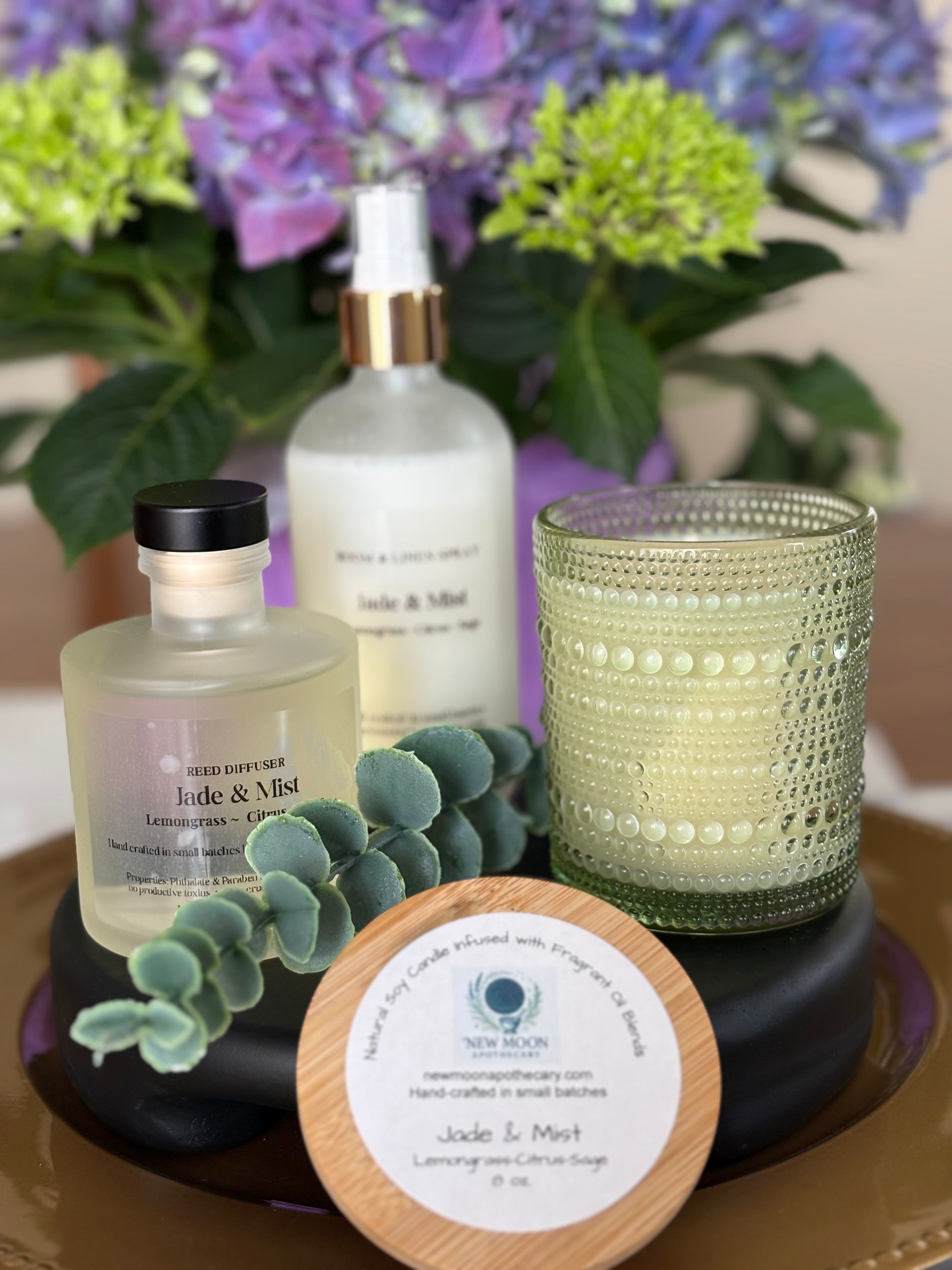 Aromatherapy products including a diffuser, bottle, candle, and coaster on a table with flowers in the background.