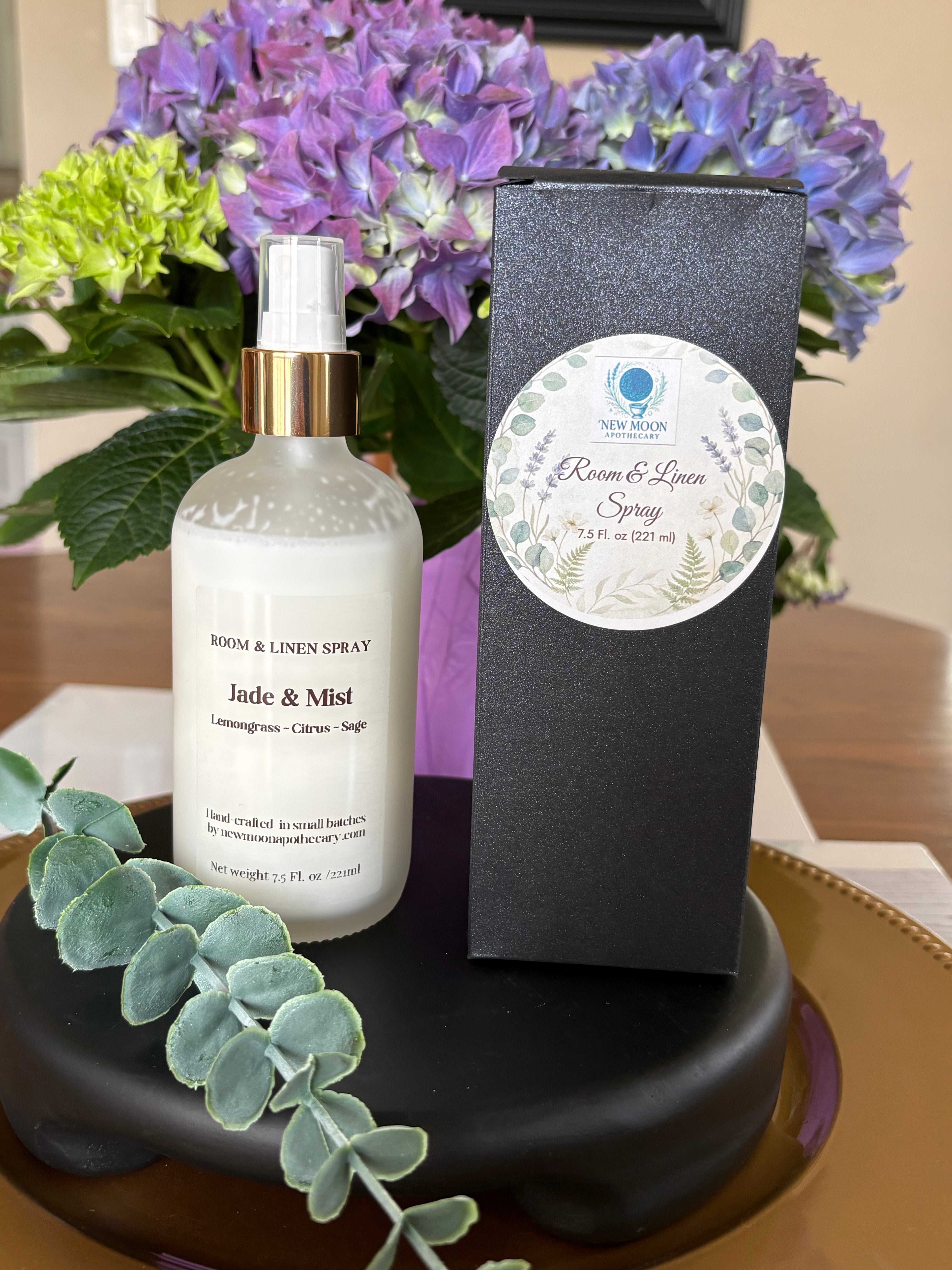 Room and linen spray bottle with packaging on a table with flowers in the background