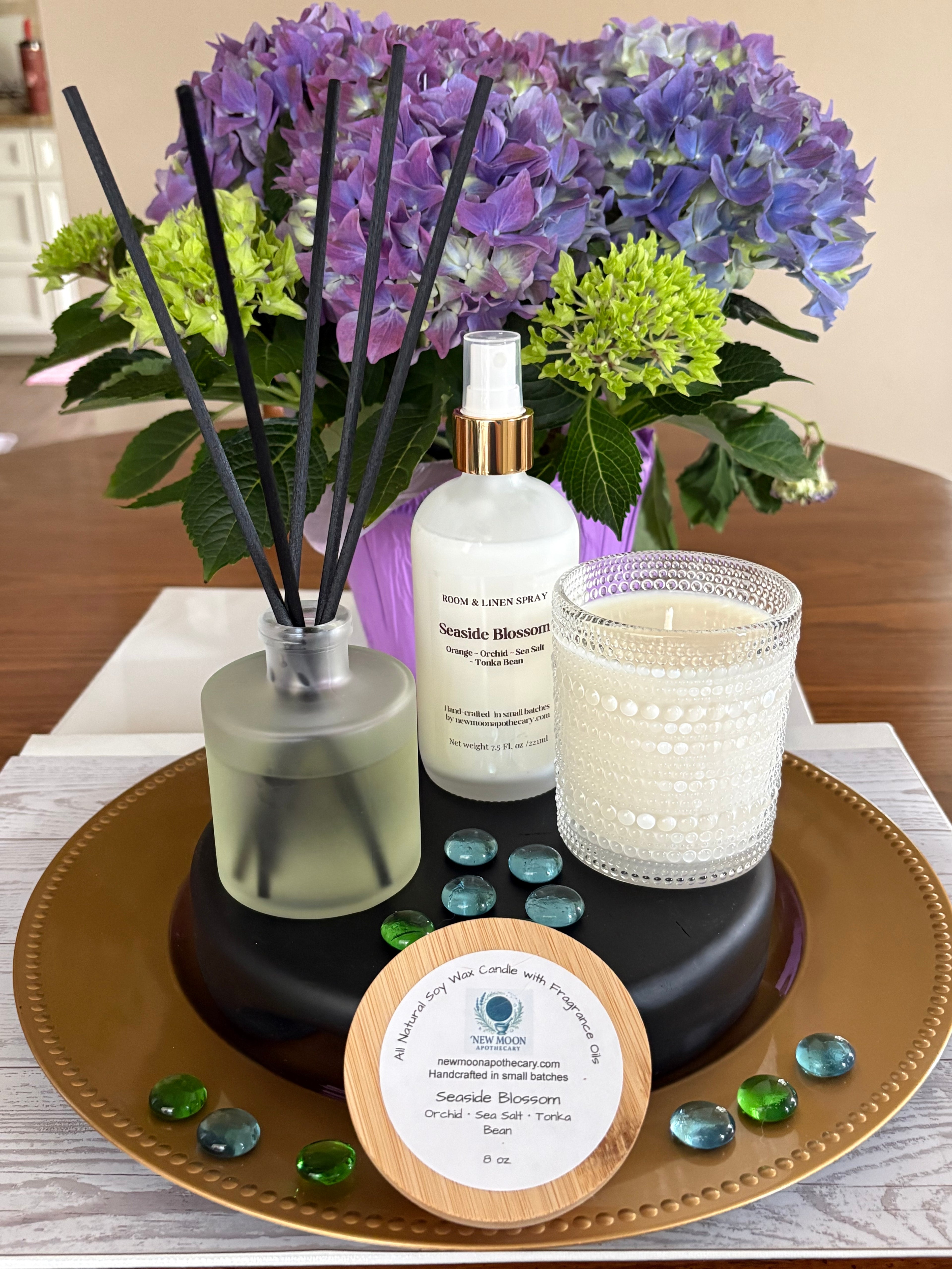 Sacred Space Collection display — reed diffuser, room spray, soy candles, glass beads, and fresh flowers styled on a wooden surface | New Moon Apothecary