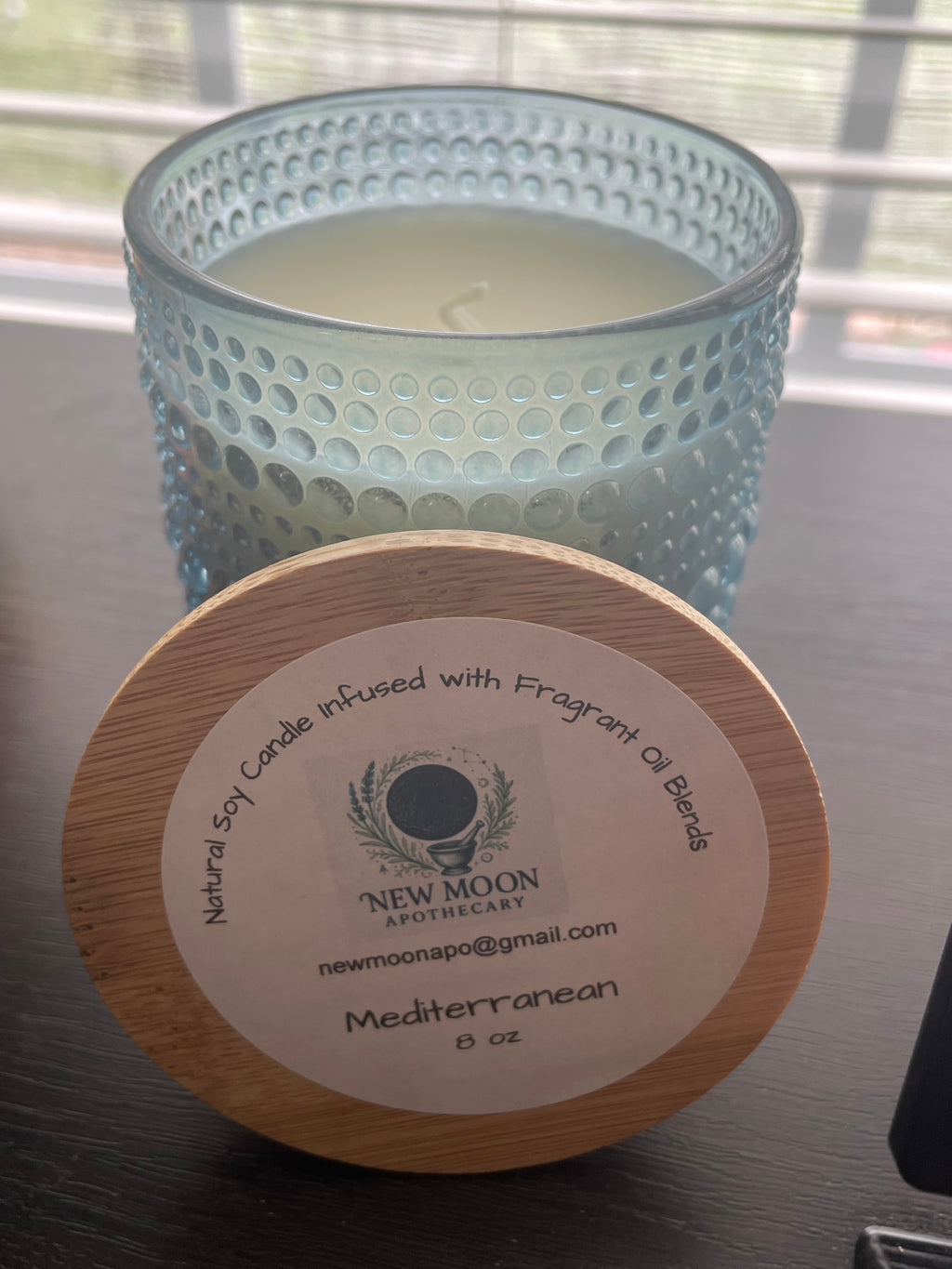 Sacred Space Soy Candle — Mediterranean scent in blue textured glass vessel with wooden lid on reflective surface | New Moon Apothecary