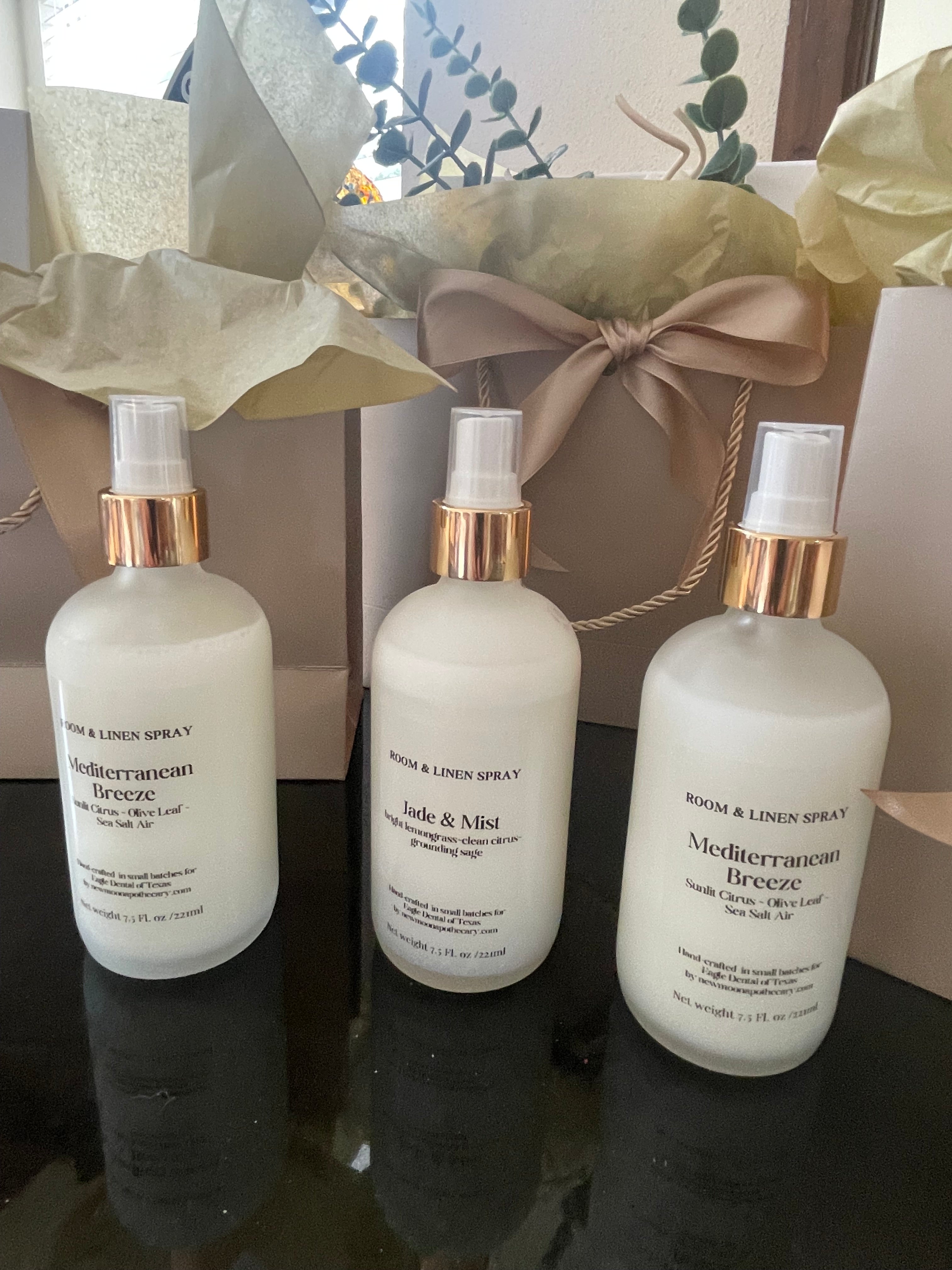 Three white bottles with gold caps on a dark surface, with a decorative bow and tissue paper in the background--New Moon Apothecary