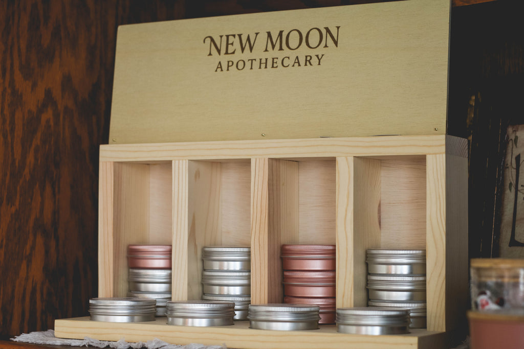 Wooden display box with New Moon Apothecary branding, containing small containers.