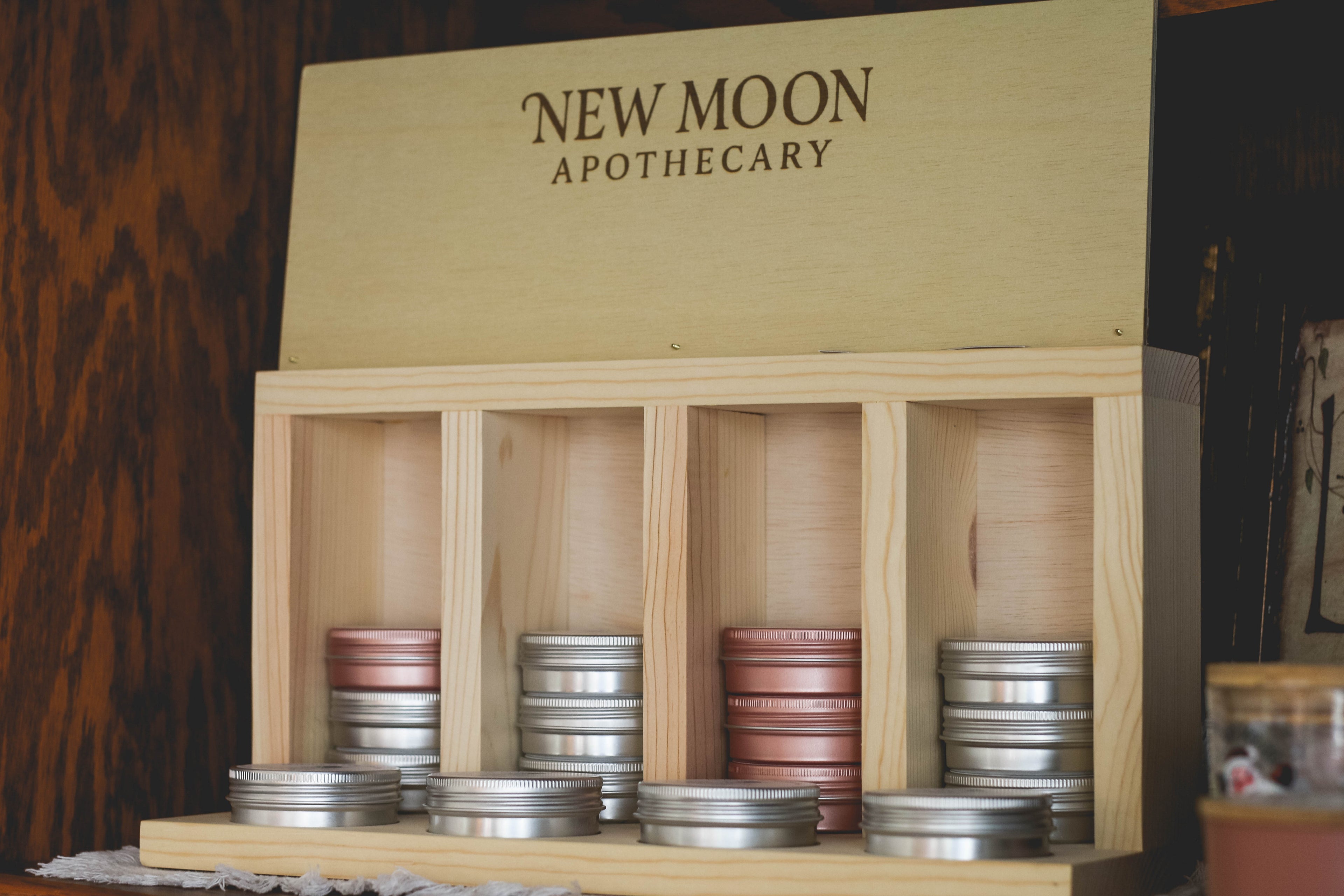 Wooden display box with New Moon Apothecary branding, containing small containers.